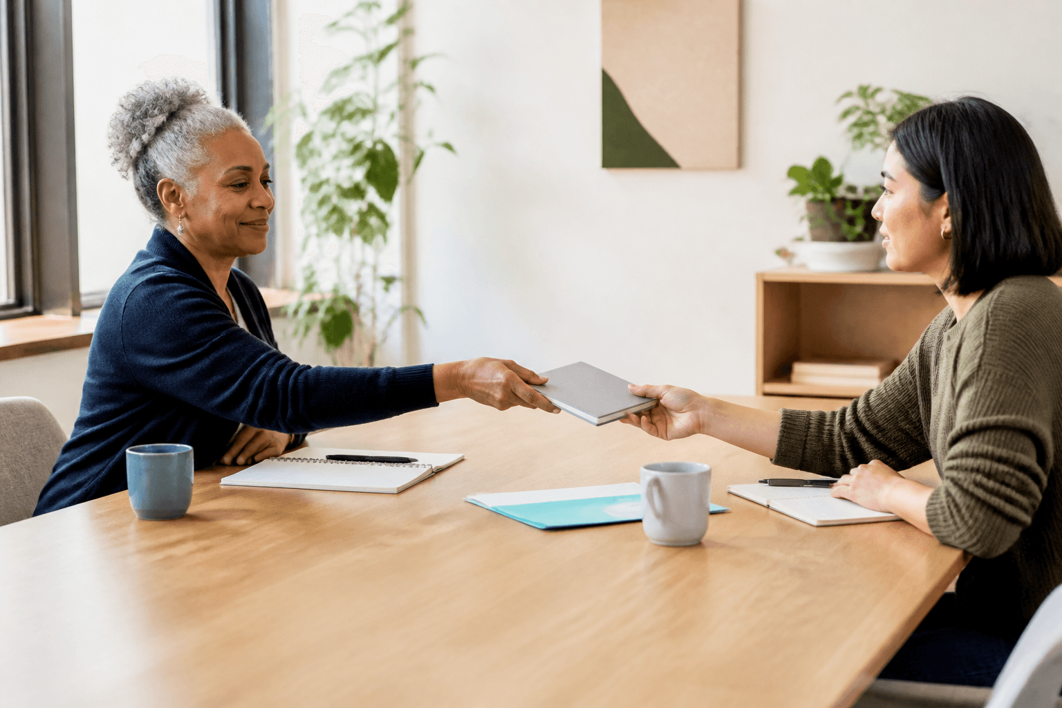Two nonprofit leaders passing a notebook across a shared table.
